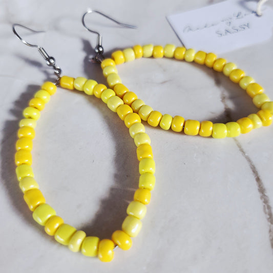 Yellow beaded hoop earrings on a marble surface with a tag.