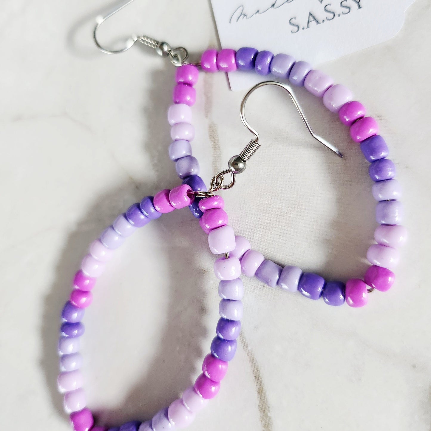 Beaded hoop earrings with pink and purple beads on a white background