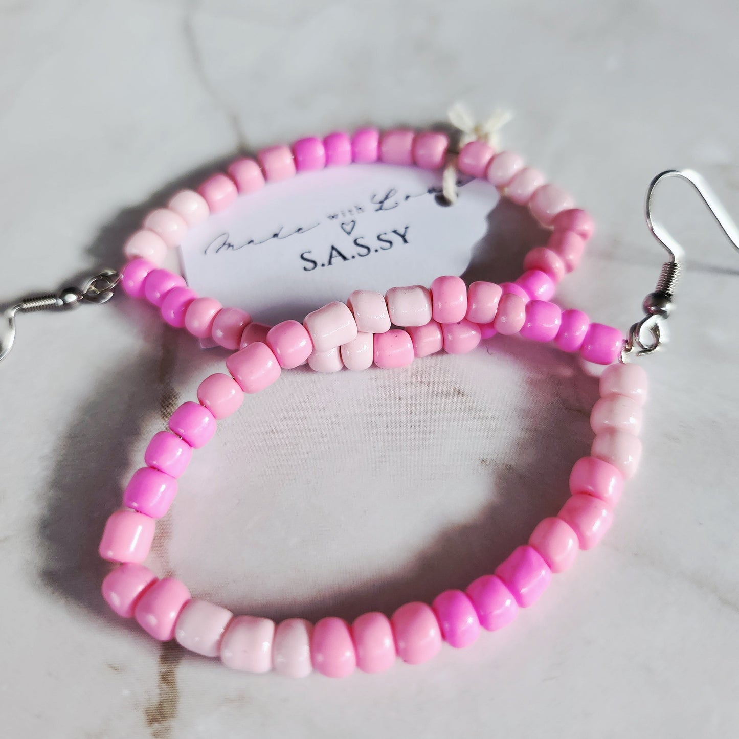 Pink beaded hoop earrings on a marble surface with a 'SASSY' card.