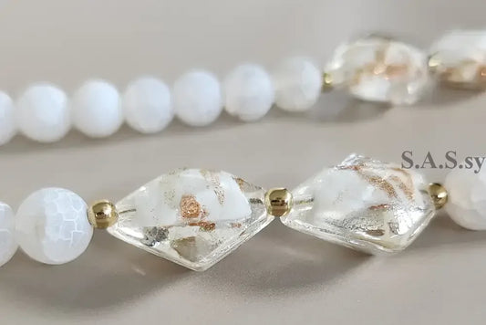 Necklace with white gemstone beads and gold accents on a grey background.