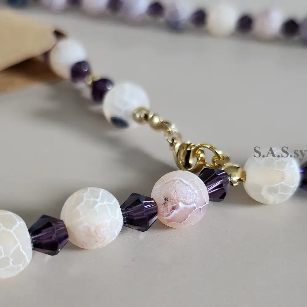 Close-up of a beaded necklace with white and purple beads on a neutral background