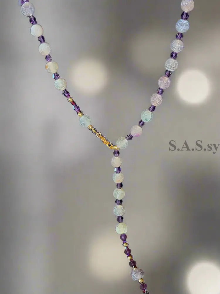 Necklace with purple stone beads on a black stand with a visible brand tag.