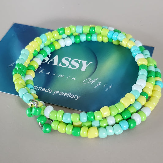 Green and blue beaded coil bracelet on a blue card with 'BASSY' branding.