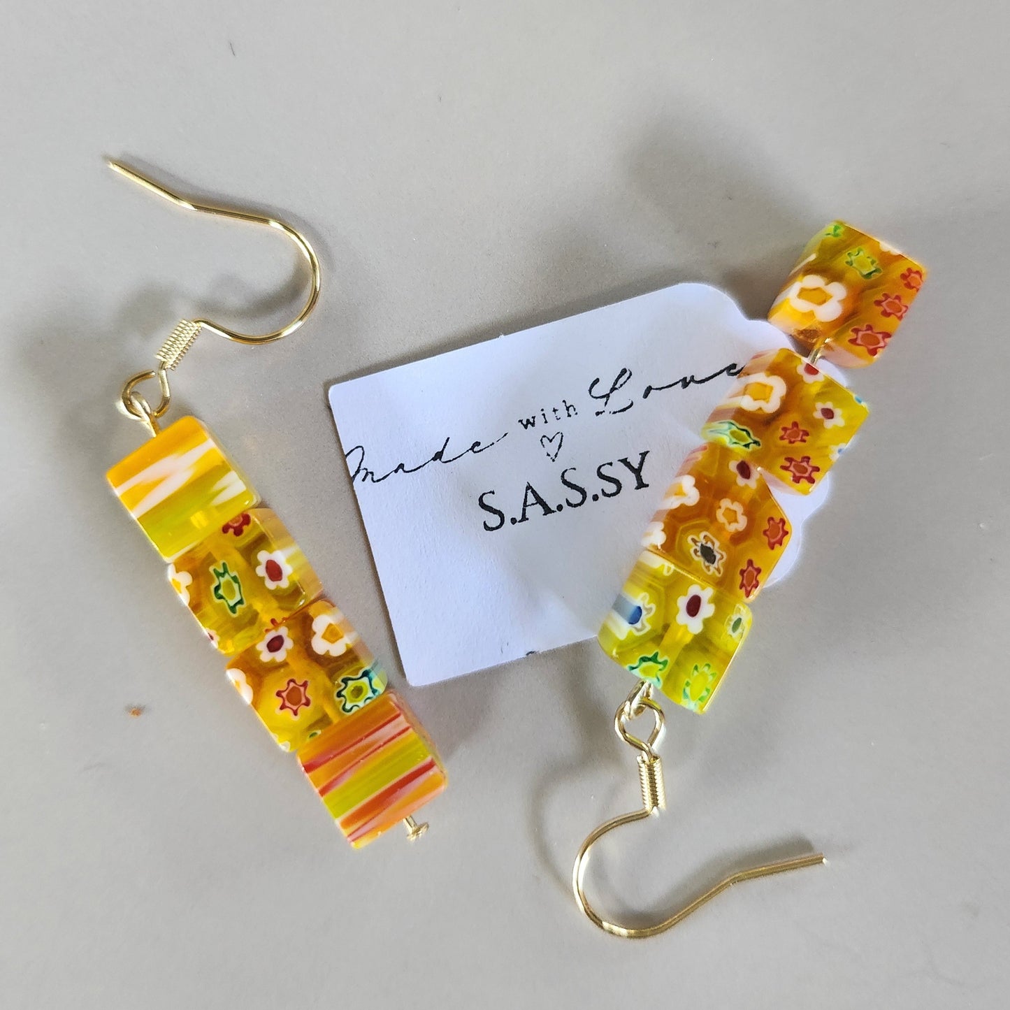 Colorful floral earrings with a 'SASSY' tag on a light gray background
