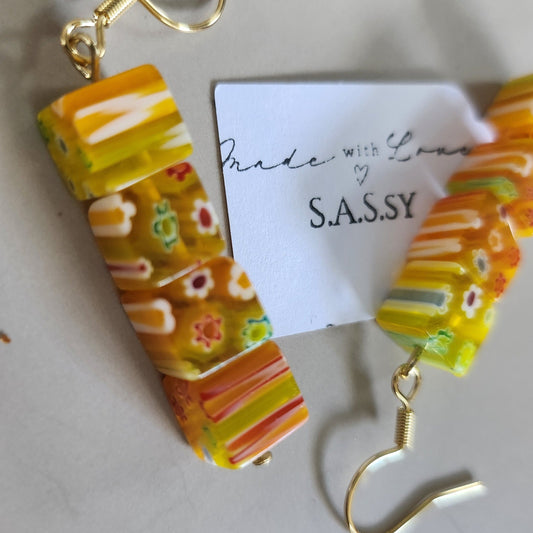 Colorful striped earrings with gold hooks on a white background, featuring the brand 'SASSY'.