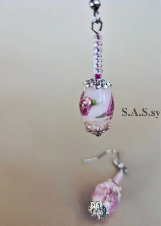 Pink floral glass bead drop earrings with silver-tone hooks and rhinestone accents, shown against a plain beige background.