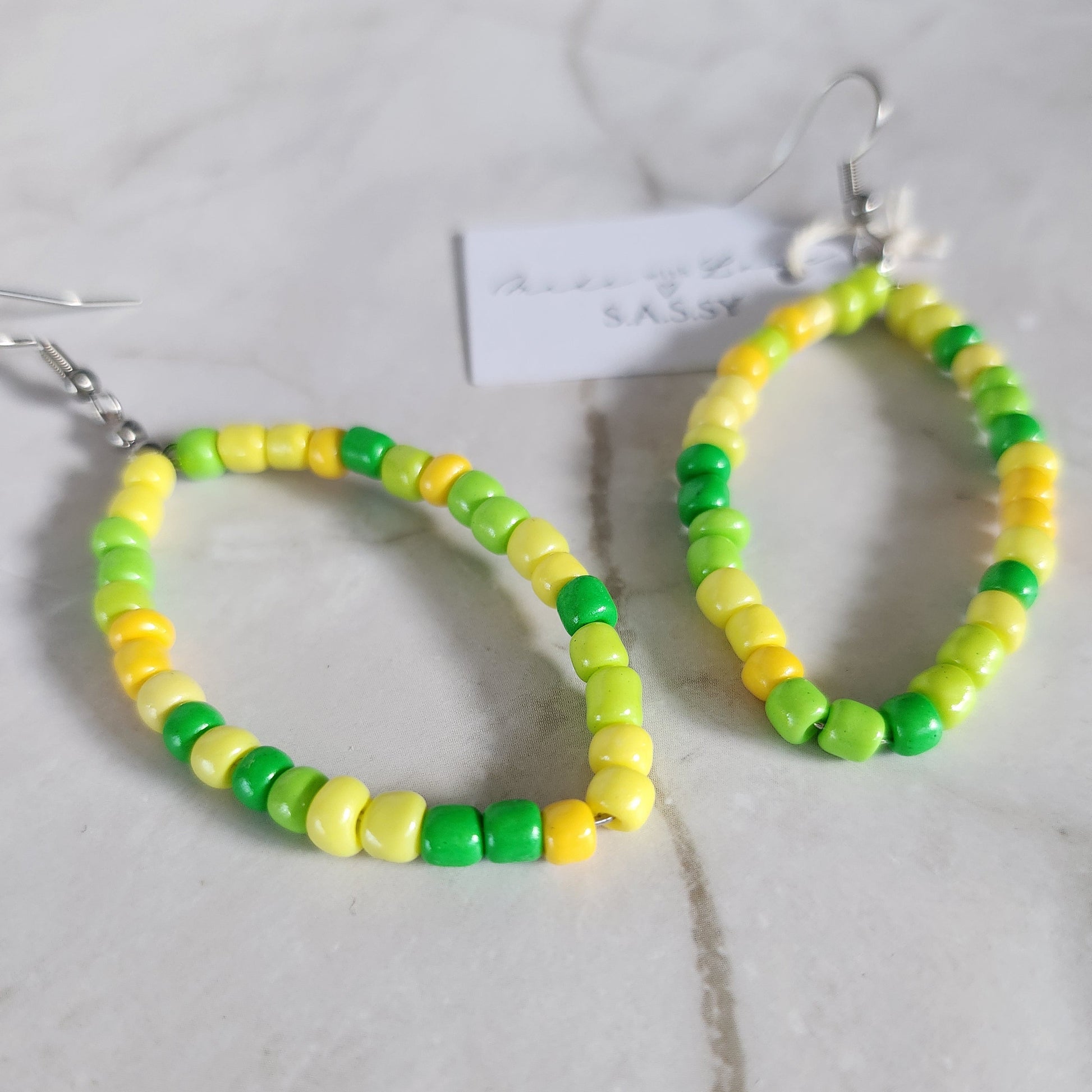 Yellow and green beaded hoop earring on a light gray surface