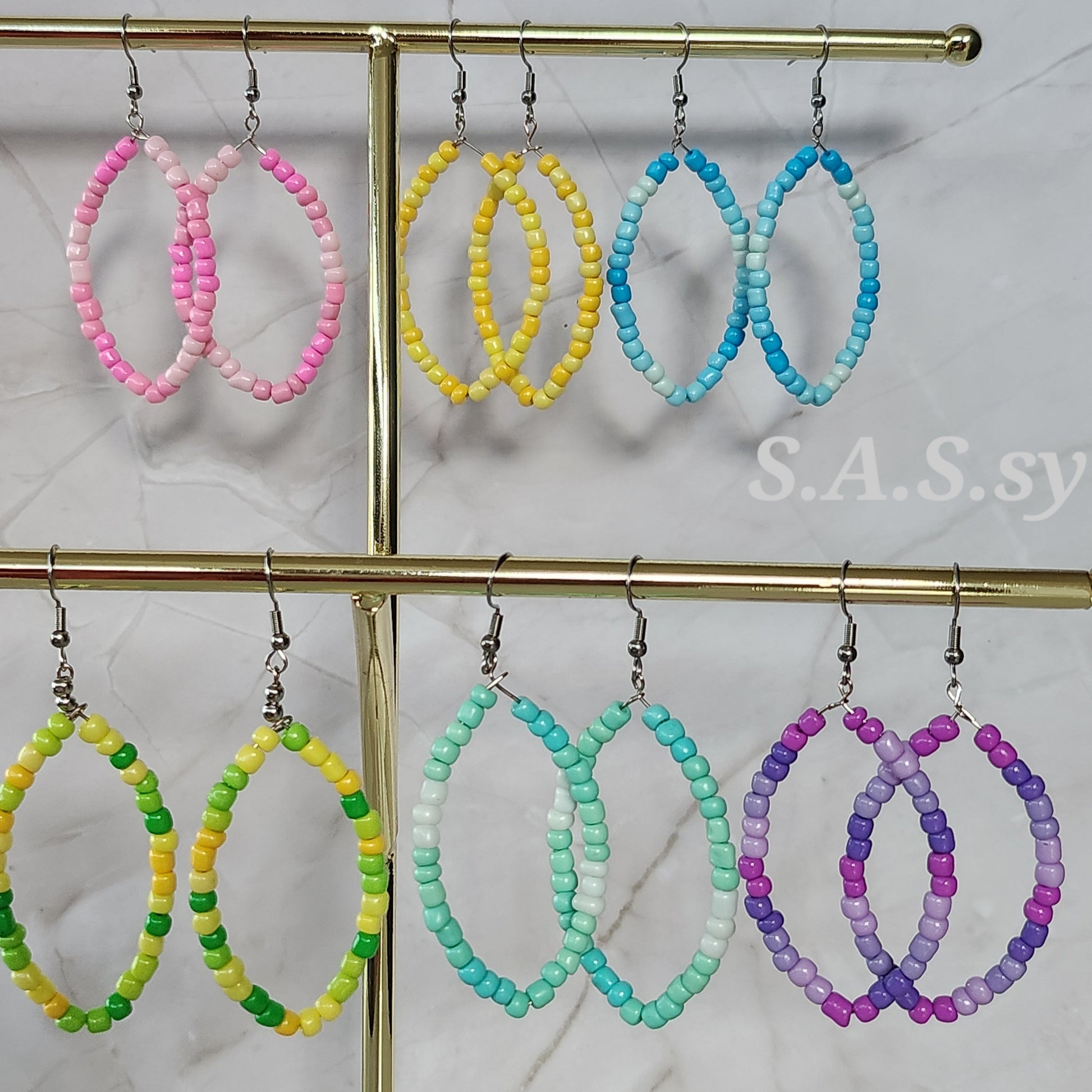 Colorful beaded hoop earrings on a gold stand with a marble background