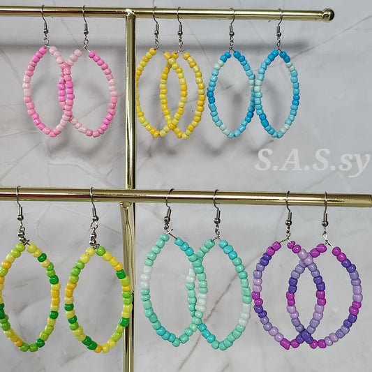 Colorful beaded hoop earrings on a gold stand with a marble background