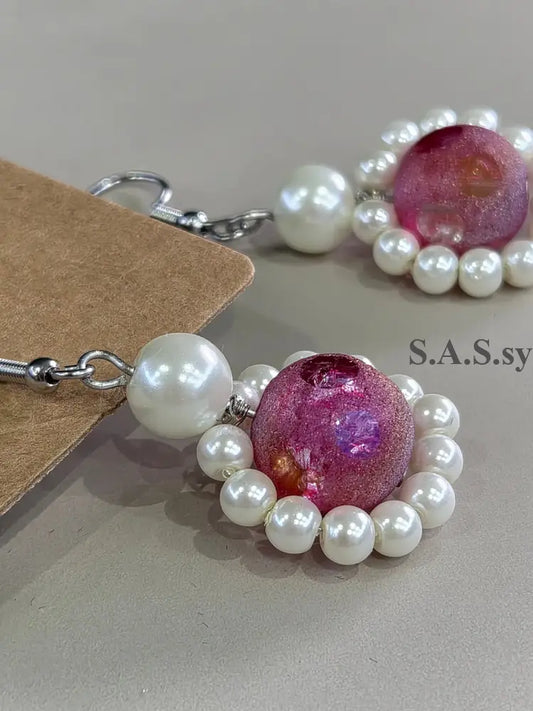 Pair of earrings with purple gemstones and white pearls on a neutral background