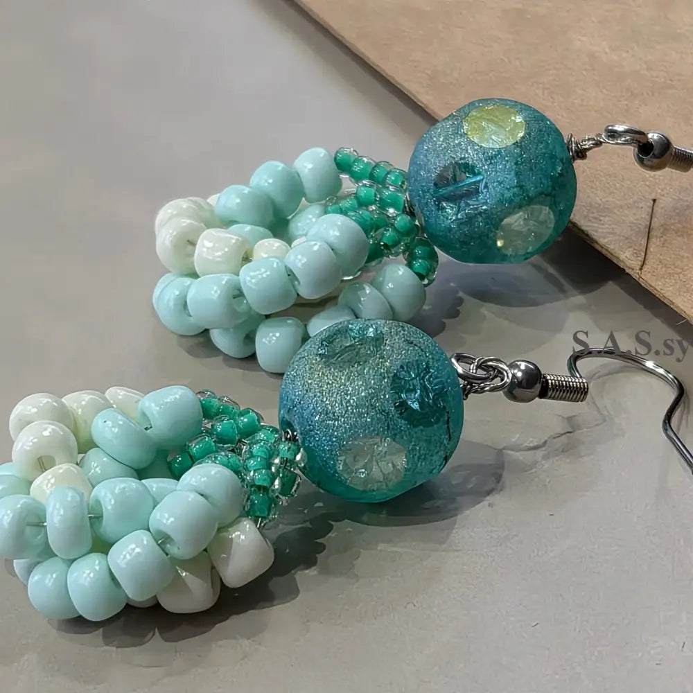 Green and white beaded earrings on a neutral background