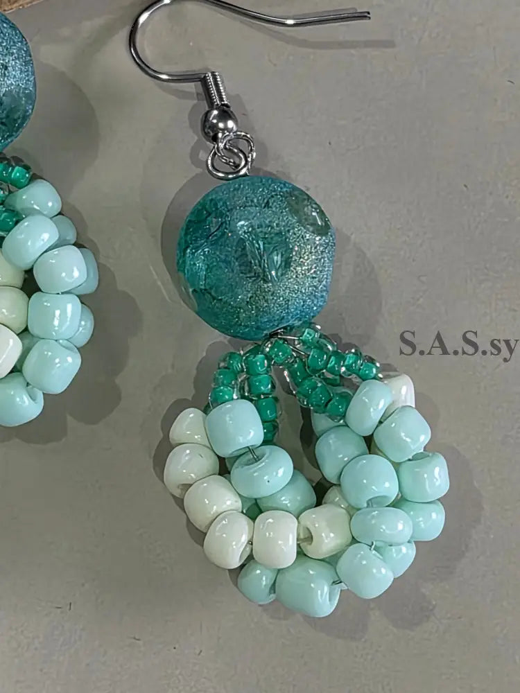 Beaded earrings with turquoise, green, and white beads on a gray background