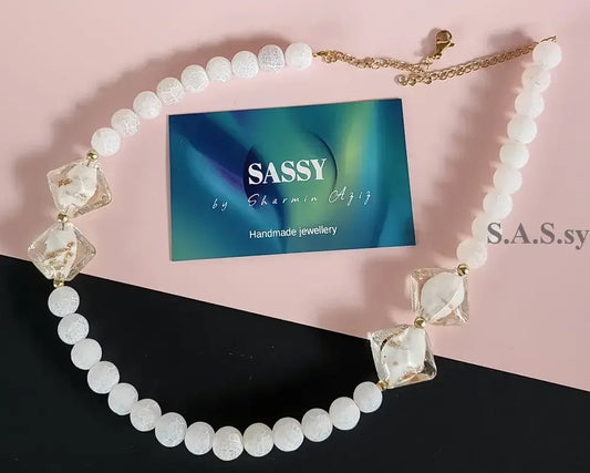 Necklace with white gemstone beads and gold accents on a pink and black background.