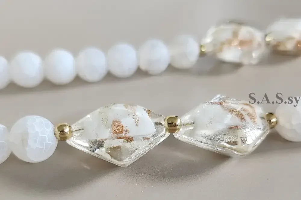 Necklace with white gemstone beads and gold accents on a grey background.