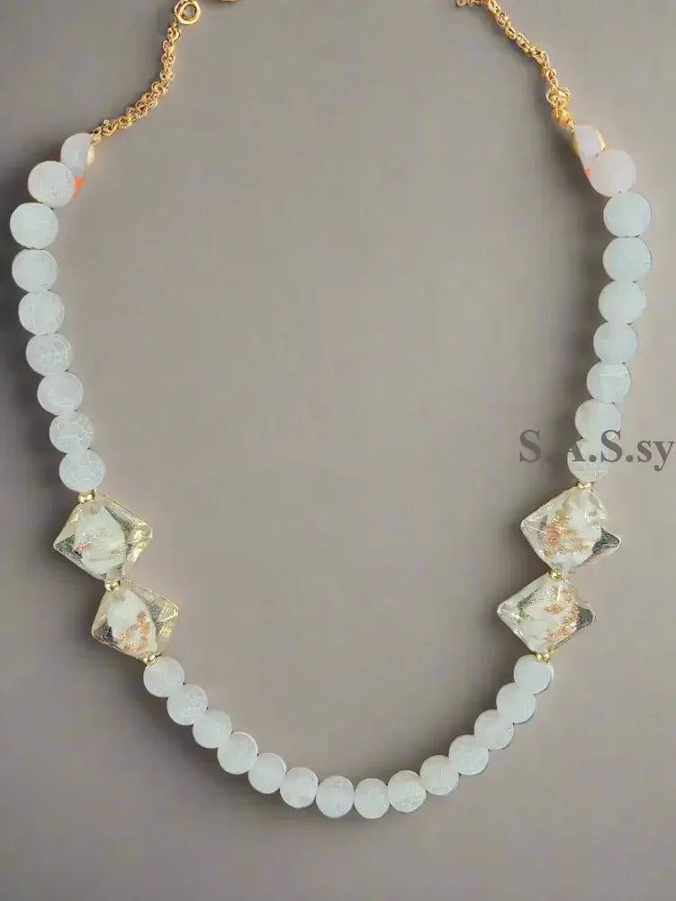 Necklace with white gemstone beads and gold accents on a grey background.