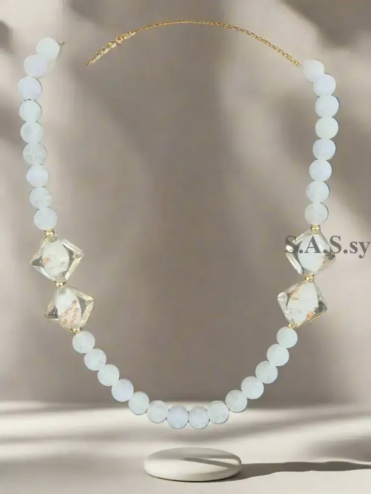 Necklace with white gemstone beads and gold accents on a grey background.