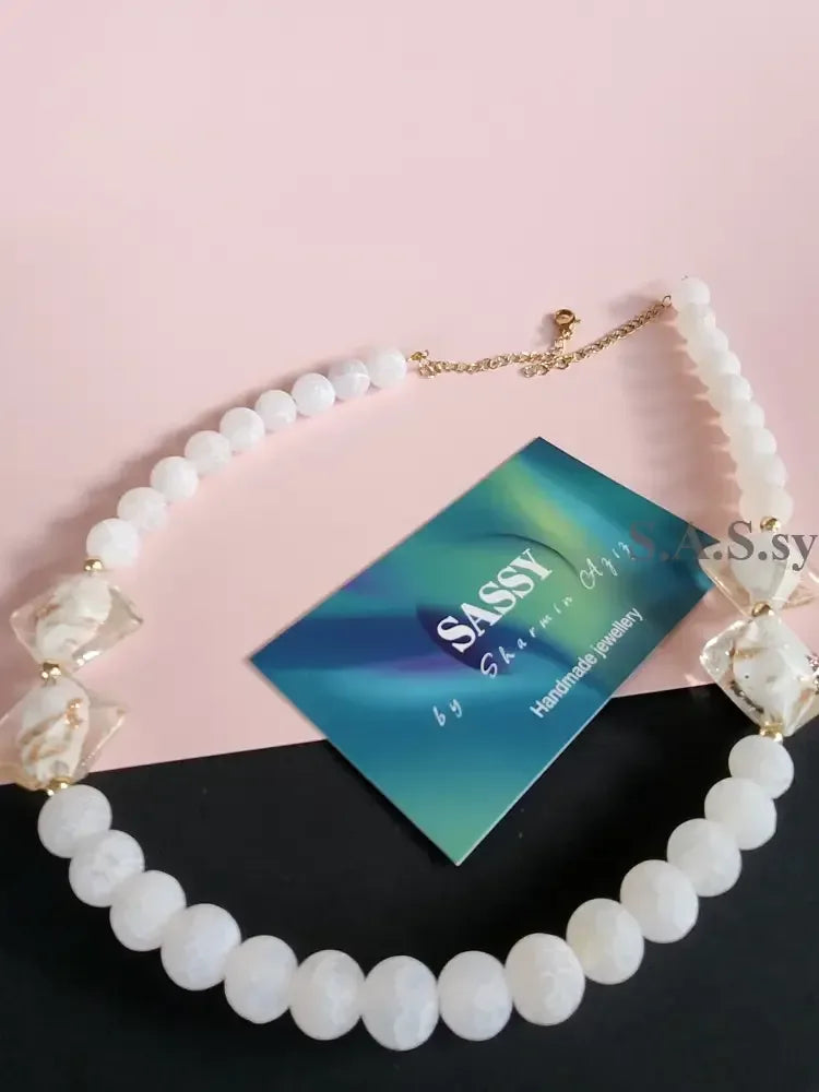 Necklace with white gemstone beads and gold accents on a pink background.