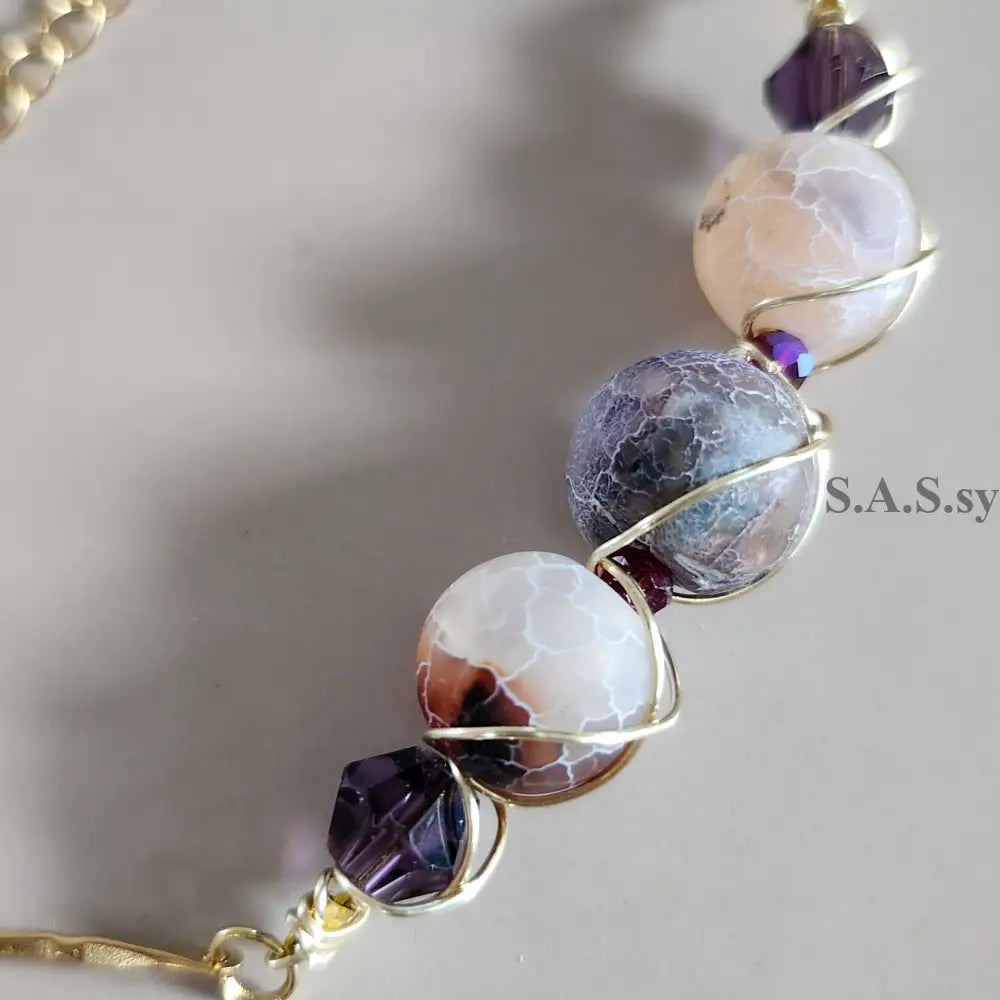 Close-up of a beaded  gemstone bracelet with gold chain on a gray background