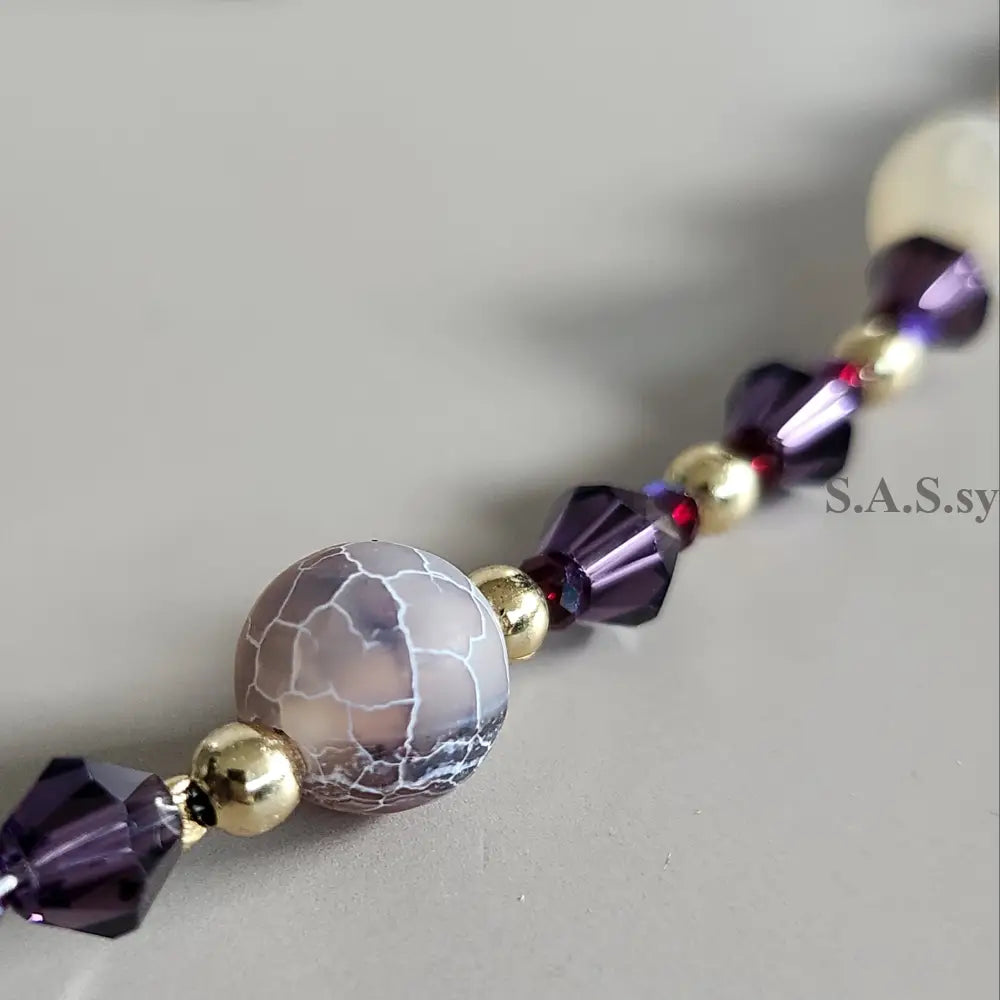 Close-up of a beaded necklace with purple and gold beads on a neutral background