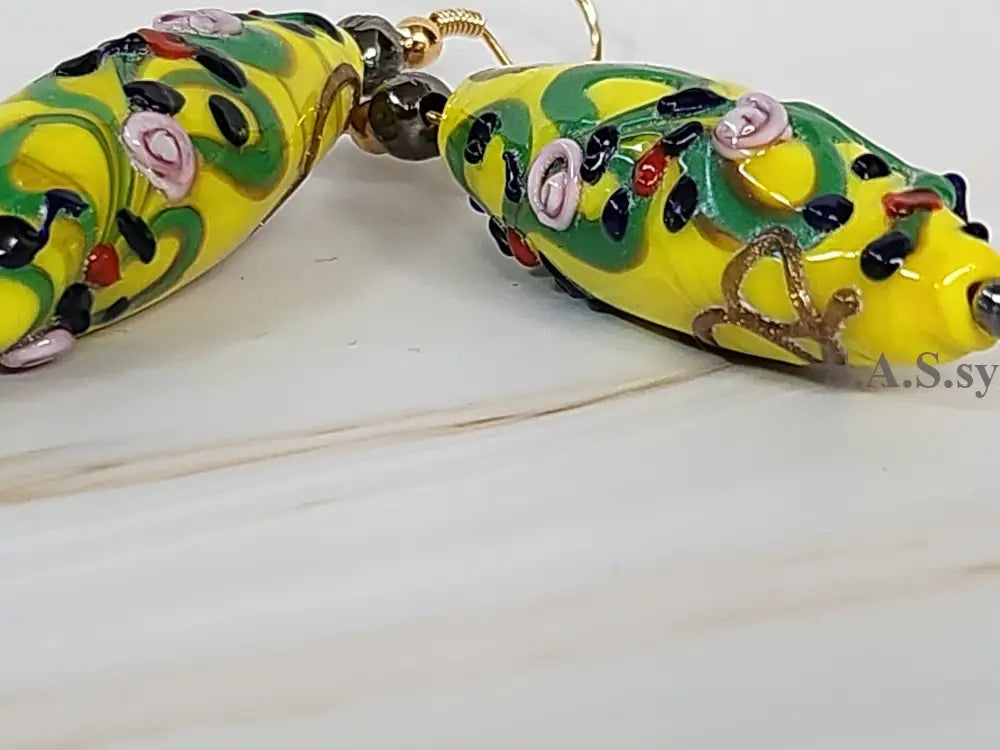 A pair of yellow, green and black beaded earring on a marble surface