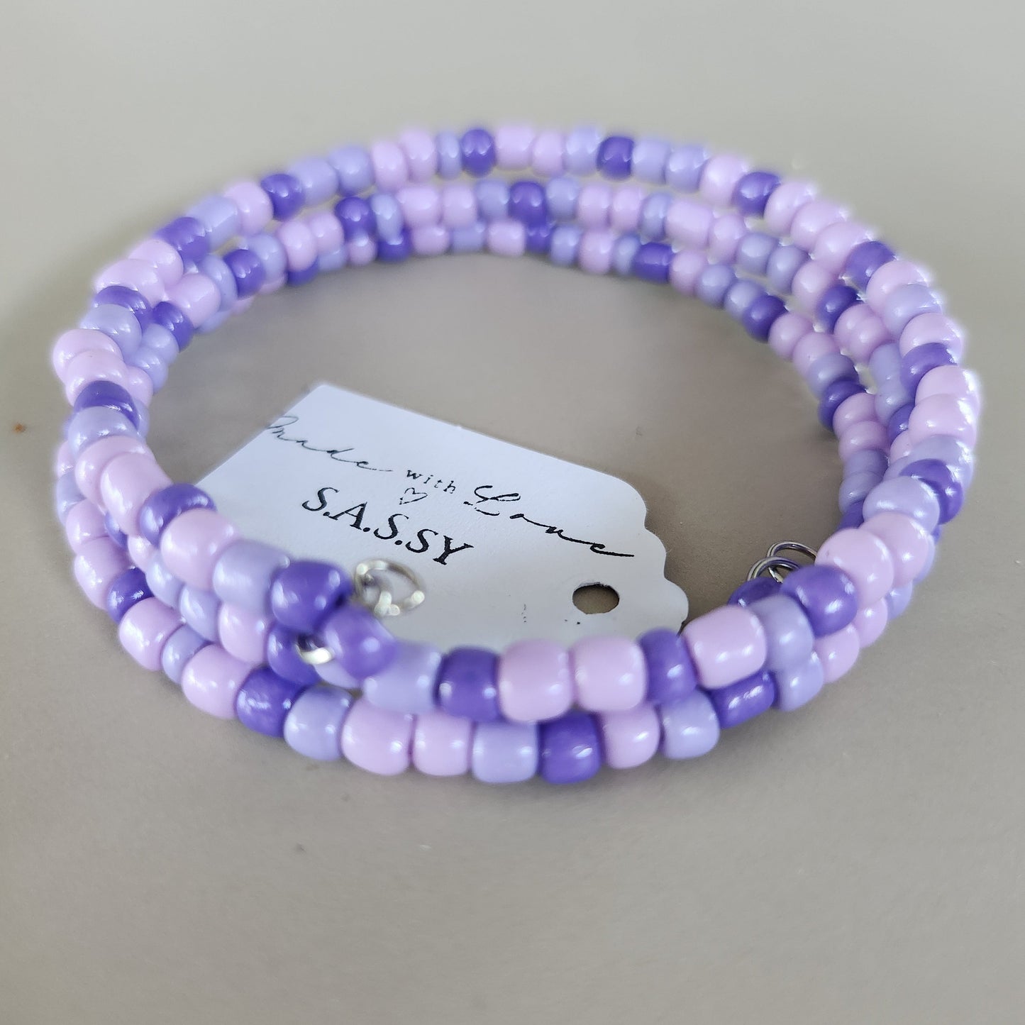 Purple beaded bracelet with a tag on a light gray background