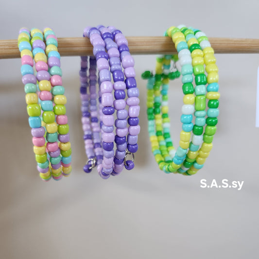 Colorful beaded bracelets on a wooden stick with 'S.A.S.sy' branding.