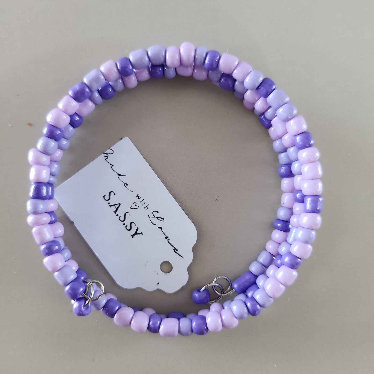 Purple and white beaded bracelet with a tag on a beige background