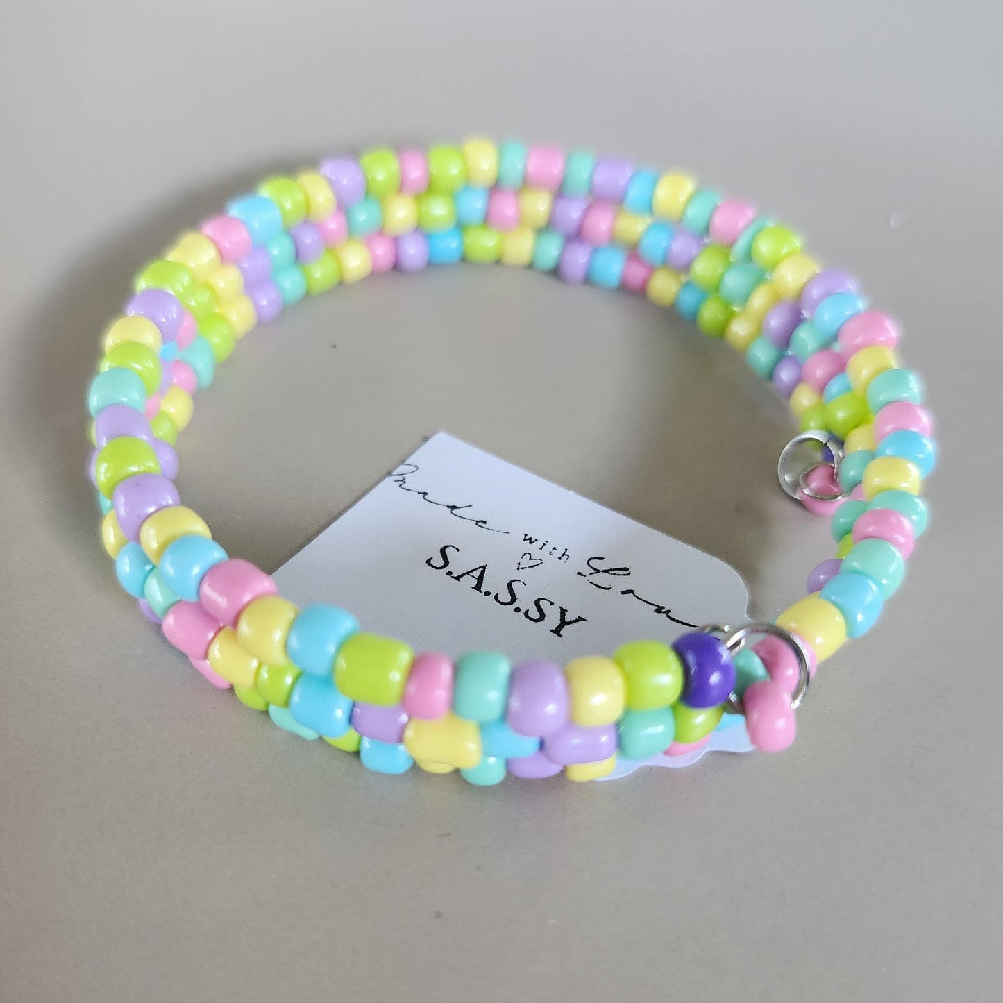 Colorful beaded bracelet with a 'SASSY' tag on a light gray background