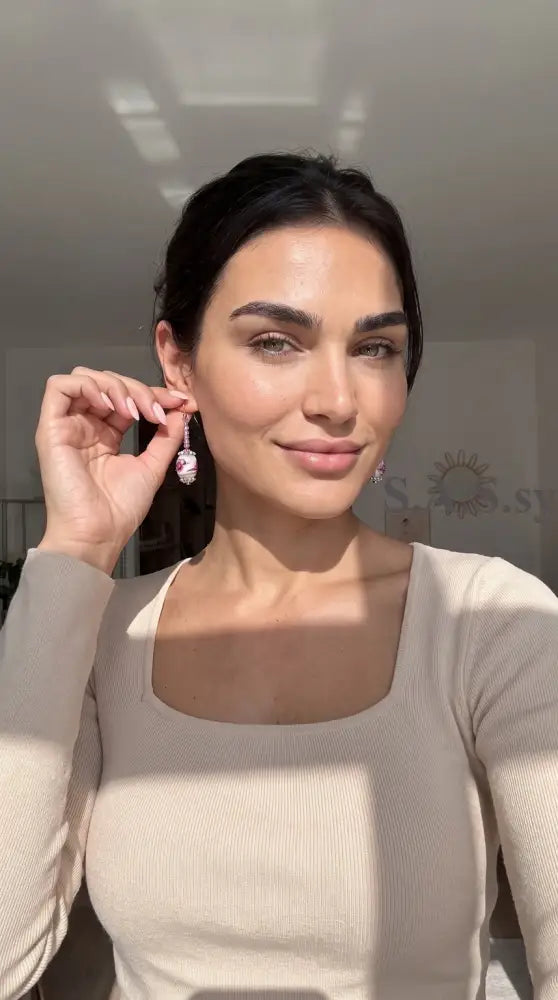  Woman wearing a pair of handmade dangle earrings featuring oval pink and white floral lampwork beads with silver wire-wrapped hooks.